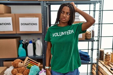 Young african american woman working wearing volunteer t shirt at donations stand confuse and wondering about question. uncertain with doubt, thinking with hand on head. pensive concept.