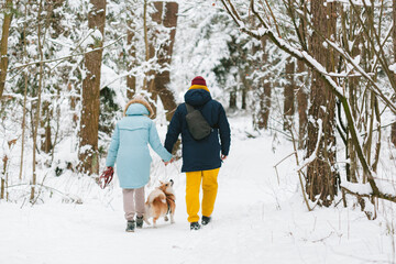 Fototapeta na wymiar Well dressed happy girl and man with Corgi dog outdoors in winter. Pets, people and season concept. Cheerful couple having fun with cute dog in snowy park