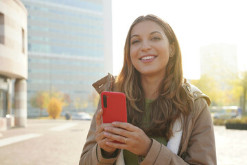 Young confident woman using smartphone over city background smiling and looking at camera