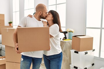 Fototapeta na wymiar Young hispanic couple kisisng and holding cardboard box at new home.