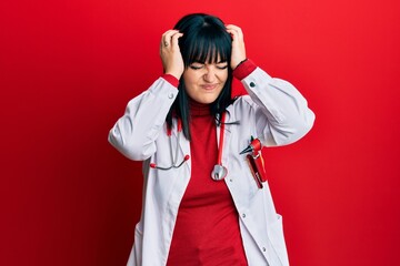 Young hispanic woman wearing doctor uniform and stethoscope suffering from headache desperate and stressed because pain and migraine. hands on head.