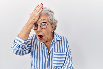 Senior woman with grey hair standing over white background surprised with hand on head for mistake, remember error. forgot, bad memory concept. - obrazy, fototapety, plakaty