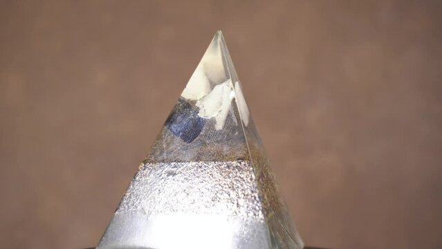 Orgonite Crystal Pyramid Rotating Against Bokeh Background. Close Up