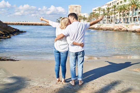 Middle age man and woman couple on back view hugging each other and kissing with arms open at seaside