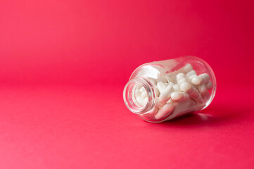 an open glass jar with pill capsules lies on a red background, copy space.