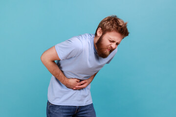 Stomach pain. Side view of bearded man standing and holding his painful belly, feeling bad,...
