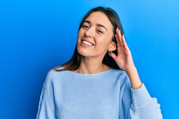 Young hispanic girl wearing casual clothes smiling with hand over ear listening an hearing to rumor or gossip. deafness concept.