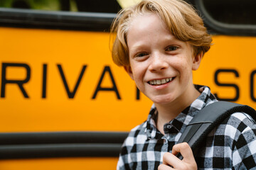 White boy with backpack smiling while standing by school bus