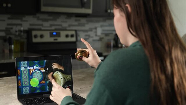 Smiling woman takes remote lesson to learn finger cymbals online on a laptop. Remote learning concept.