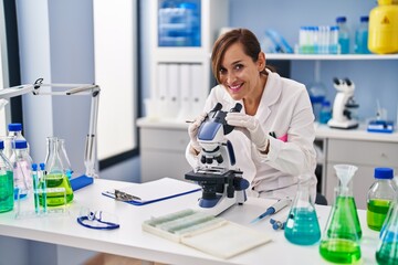 Middle age woman wearing scientist uniform using microscope at laboratory