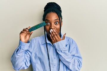 African american woman with braided hair holding ram memory covering mouth with hand, shocked and...