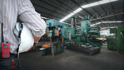 Fototapeta premium Rear view image of foreman checking and control loading work with walkie talkie radio&nbsp;and holding hard safety helmet. Architect standing and looking at heavy industry manufacturing factory background