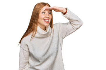 Young irish woman wearing casual winter sweater very happy and smiling looking far away with hand over head. searching concept.