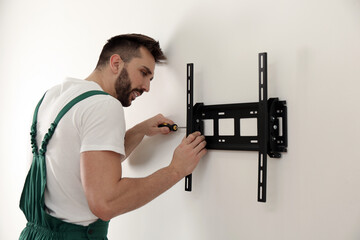 Professional technician with screwdriver installing TV bracket on wall indoors