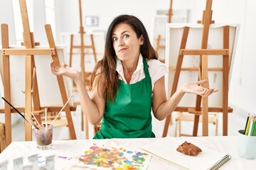 Beautiful caucasian woman at art studio clueless and confused expression with arms and hands...