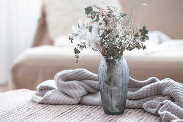 Home composition with a glass vase with dried flowers on a blurred background.
