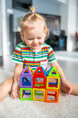 Little girl playing colorful magnet plastic blocks kit at home. The child playing educational...
