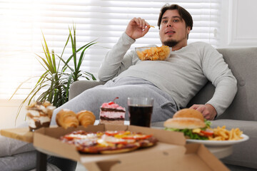 Overweight man with chips on sofa at home