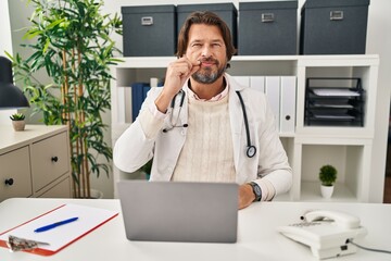 Handsome middle age doctor man working at the clinic mouth and lips shut as zip with fingers....