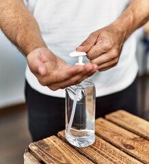 Young hispanic man customer cleaning hands using sanitizer gel at clothing store