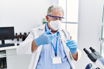 Middle age grey-haired man wearing scientist uniform using syringe at laboratory