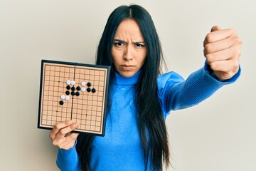 Young hispanic girl holding asian go game board annoyed and frustrated shouting with anger, yelling...