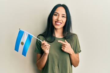 Young hispanic girl holding argentina flag smiling happy pointing with hand and finger - obrazy, fototapety, plakaty