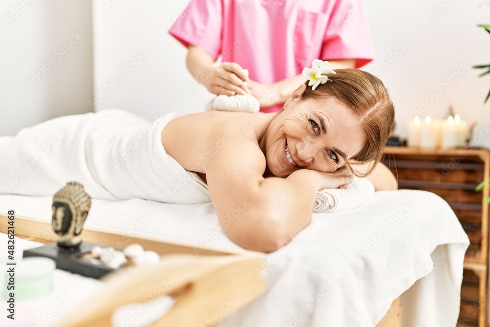 Poster Middle age caucasian woman having back massage using thai hot bags at beauty center