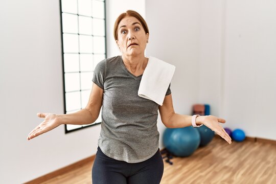 Middle age woman wearing sporty look training at the gym room clueless and confused with open arms, no idea concept.