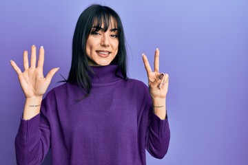 Young brunette woman with bangs wearing turtleneck sweater showing and pointing up with fingers...