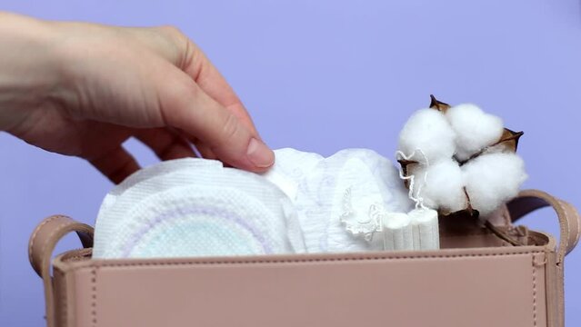 Women's hand takes out panty liner from pink cosmetic bag with tampons and feminine sanitary pads