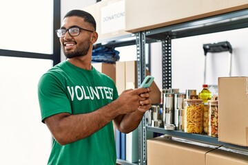 Young arab man wearing volunteer uniform using smartphone at charity center