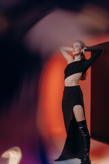 a beautiful girl in a black top, black skirt and black boots on a red background in the photo there may be noises