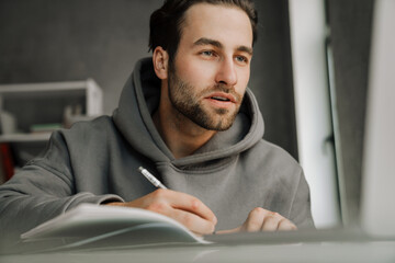 Young beard man working with laptop while writing down notes