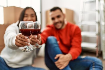 Young latin couple smiling happy toasting with red wine at new home