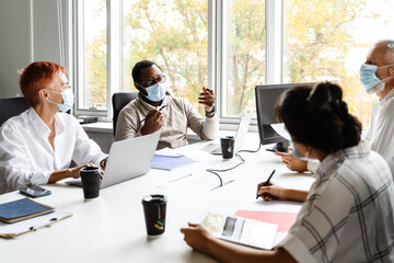 Multiracial colleagues in face masks talking during meeting at office
