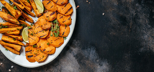 Sweet potato fries with herbs on dark background. Long banner format. top view