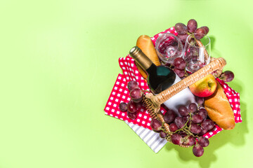 Picnic basket with food, wine bottle, glasses and fruits on green sunny lawn grass 