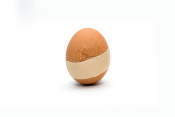 A broken egg with a crack and medical tape glued to it. The concept of treatment and healthcare. Medical plaster on a broken chicken egg on a white background