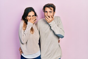 Young hispanic couple wearing casual clothes laughing and embarrassed giggle covering mouth with...