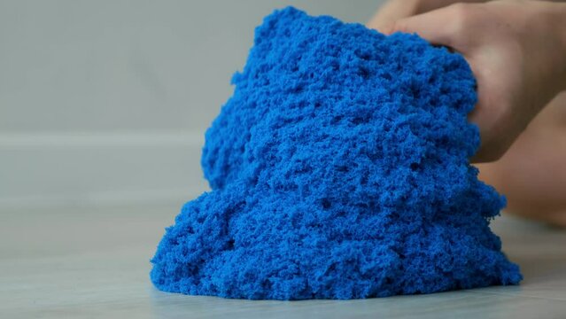 Close-up view of woman's hands with kinetic sand of bright blue color. She plays with kinetic sand stirring it in her hands. Anti-stress toy for children and adults. Sand is pouring from hands.