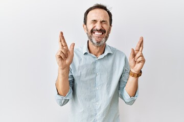 Middle age hispanic man with beard standing over isolated background gesturing finger crossed...