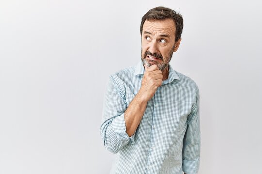 Middle age hispanic man with beard standing over isolated background thinking worried about a question, concerned and nervous with hand on chin