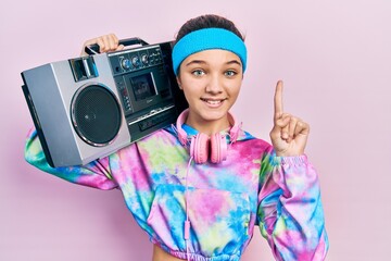 Young brunette girl wearing workout clothes and holding boombox smiling with an idea or question...
