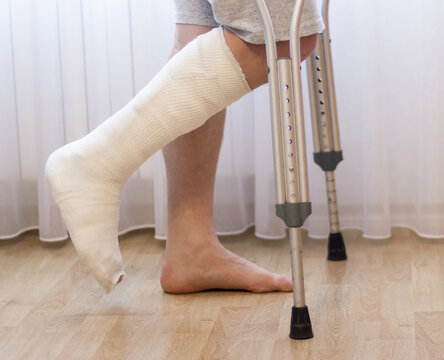 Close-up of man leg in plaster cast using crutches while walking.