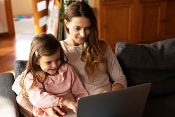 Cheerful little girl using laptop. Beautiful girl watching cartoon with mom..