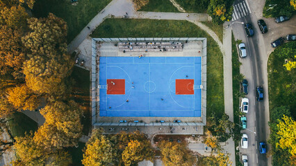 Top view of the blue stadium in the park, teenagers playing basketball in autumn