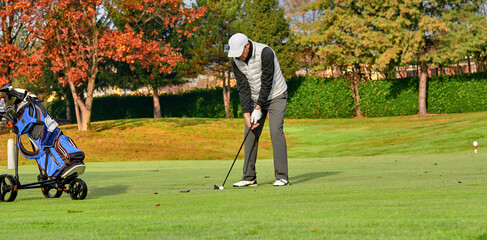 Golfer on a golf course in winter with wet grass, hitting the ball with a golf club.