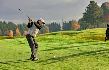 Golfer on a golf course in winter with wet grass, hitting the ball with a golf club.