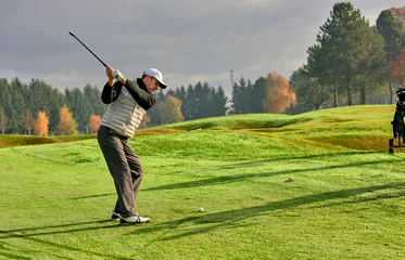 Poster Golfer on a golf course in winter with wet grass, hitting the ball with a golf club. © trattieritratti
